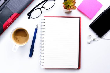 Üst görünüm ya da Düz görünüm iş için iş alanı için dizüstü bilgisayar, kalem, defter, kahve fincanı, gözlük, cep telefonu ve kulaklık beyaz masa zemininde.