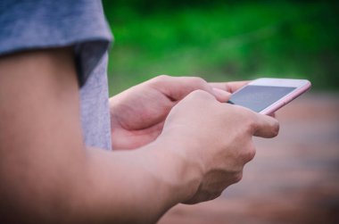 Bir adamın elinin yakın çekimi, bulanık orman manzarasına karşı fotokopi ekranıyla cep telefonu tutmaktır..
