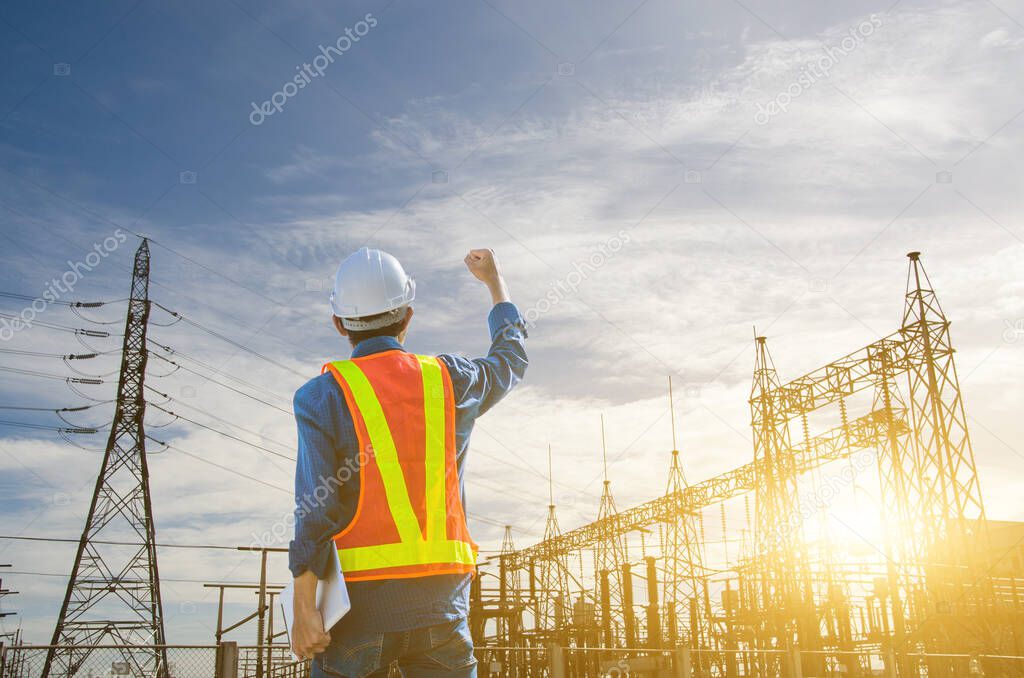 Successful engineer standing at the power substation against the sunrise background.