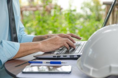 İş adamı, bir dizüstü bilgisayarda çalışıyor. Ahşap bir zeminde ve açık havada, parkta oturuyor.