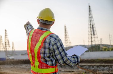 İnşaat mühendisi, inşaat alanının arka planıyla eli işaret ediyor.