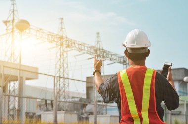 Elektrik mühendisleri ellerinde cep telefonlarıyla şantiyede duruyorlar..