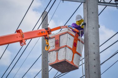 Elektrikçi, elektrik kablolarını kurmak ve onarmak için vinç sepetinin üzerinde duruyor..