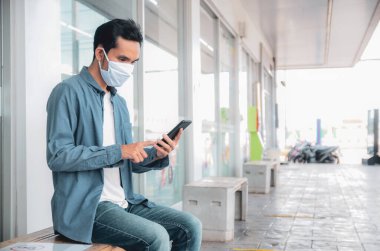 Asyalı bir adam yüz maskesi takıyordu, cep telefonunu yaşam tarzına göre tutuyordu.