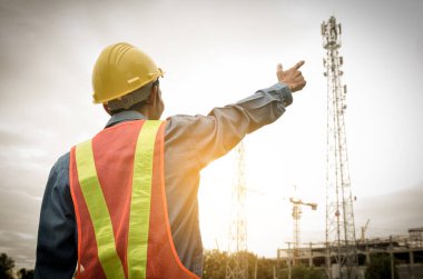 Engineer points to the telecommunication tower against the sunrise sky background