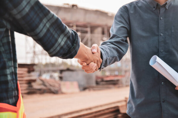 Engineers shaking hands at the construction site against the background of the bridge.