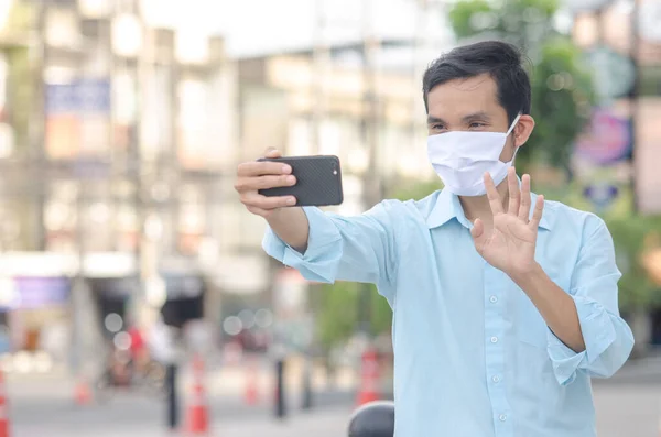 Young man in a medical mask to avoid the spread of coronavirus using VDO call smartphone in the city, social distancing, New normal concept.