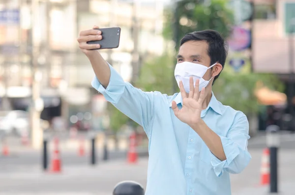Young man in a medical mask to avoid the spread of coronavirus using VDO call smartphone in the city, social distancing, New normal concept.