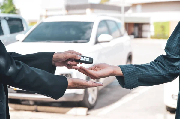 Car salesman sells a car to customer on car dealership and hands over the smart keys