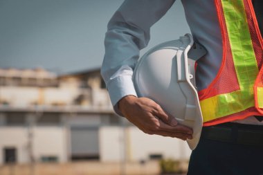 İnşaat ustabaşının elinde binanın arka planında beyaz şapka var.