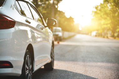 Yol kenarına park etmiş beyaz bir araba. Parlak güneş ışığı alan doğal bir geçmişi var..