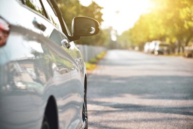 Yol kenarına park etmiş beyaz bir araba. Parlak güneş ışığı alan doğal bir geçmişi var..