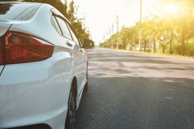 Yol kenarına park etmiş beyaz bir araba. Parlak güneş ışığı alan doğal bir geçmişi var..