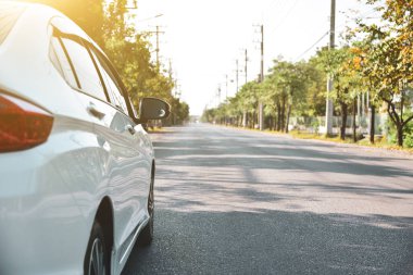 Yol kenarına park etmiş beyaz bir araba. Parlak güneş ışığı alan doğal bir geçmişi var..