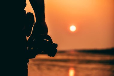 Günbatımı arka planında dijital kamerası olan doğa fotoğrafçısının silueti..