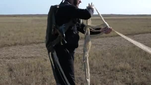 Skilled man with bag holds and reels parachute lines on hand — Stock Video