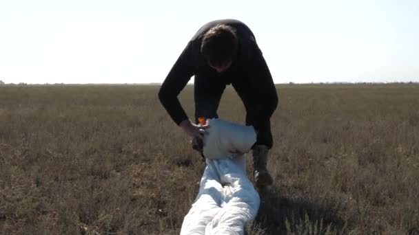 Hombre de pelo oscuro concentrado pliega primer paracaídas blanco — Vídeos de Stock