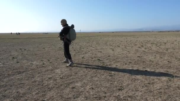 Man som bär speciella fallskärm utrustning promenader längs fältet — Stockvideo