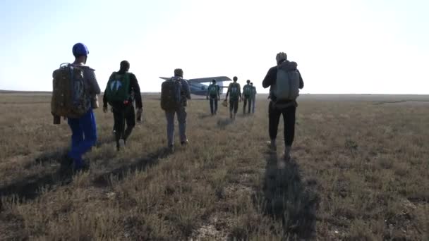 Parachutists group walks along dry airfield to airplane — Stock Video