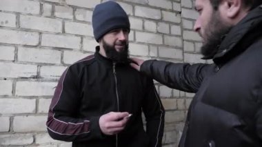Şapkalı ve sigaralı bir adam, insanı tuğla duvarın yakınına iter.