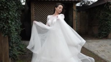 Gelinlikli kadın, duvarın yanında etekle sarmaşıkla oynuyor.