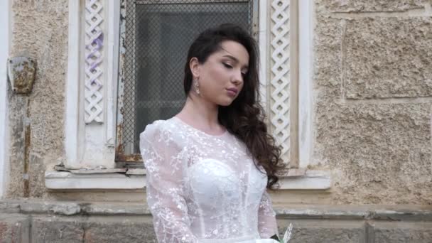 Dreamful nevěsta v bílých šatech upravuje vlasy v blízkosti staré budovy — Stock video