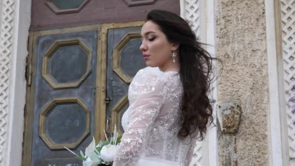 Pengantin dalam gaun cantik memegang karangan bunga dekat pintu vintage — Stok Video