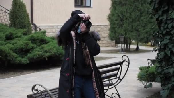 Mujer con máscara médica en chaqueta toma foto en el jardín de la ciudad — Vídeos de Stock