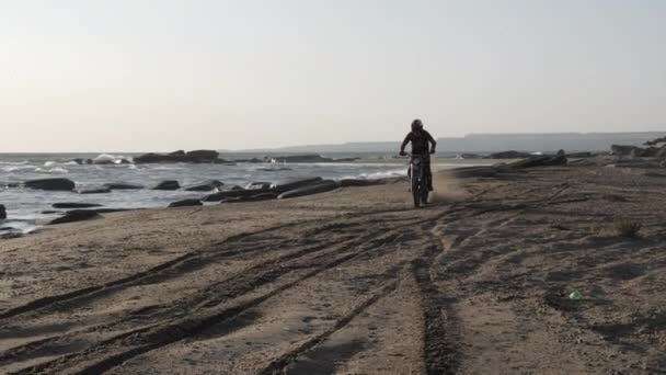 Cyklist i hjälm står på cykel och kör längs sandstrand — Stockvideo