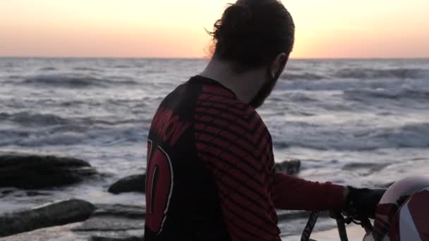 Motocycliste avec barbe tourne la tête contre la mer ondulante — Video
