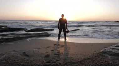 Koruyucu kasklı motorcu silueti deniz sahilinde duruyor.