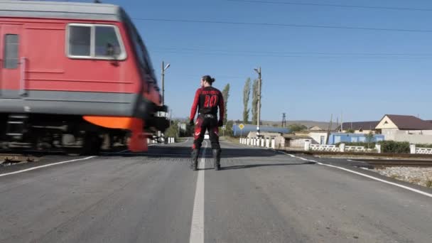 Velocidades del tren más allá del motociclista de pelo oscuro en el cruce ferroviario — Vídeos de Stock