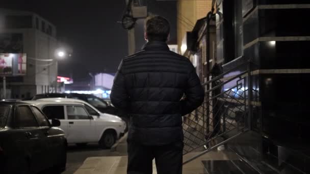 Mann in warmer schwarzer Jacke läuft auf gepflastertem Bürgersteig in Straße — Stockvideo