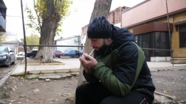 Renkli ceketli sakallı adam kibritle sigara yakıyor.