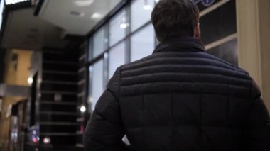 Ceketli adam kaldırımda yürür ve vitrinlere bakar.