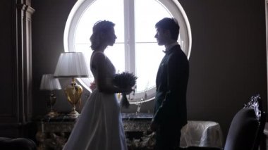 Güzel gelin ve genç damat pencerenin yanındaki kameraya poz veriyor