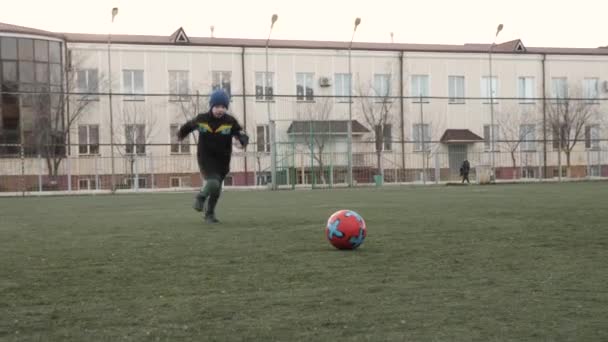 ハッピーボーイは家で緑のサッカー場でボールをキックするために実行されます — ストック動画