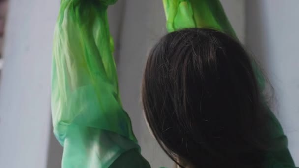 Mädchen in grünem Kleid mit Schleife auf dem Rücken am Fenster im Atelier — Stockvideo