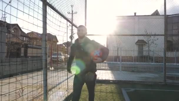 Hombre sonriente sostiene bola colorida caminando a lo largo del campo de fútbol Video de stock libre de derechos