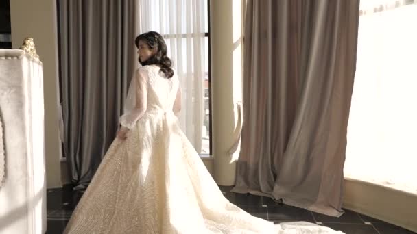 Okouzlující nevěsta v šatech s dlouhým vlakem v blízkosti velkých oken — Stock video