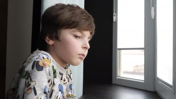 Pensive boy looks out of window leaning on sill in room — Stock Video