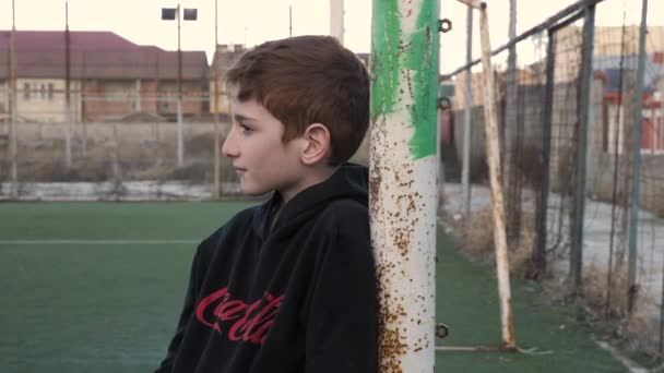 Menino feliz se inclina no poste do portão no campo de futebol Videoclipe