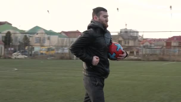Hombre feliz con pelota corre a lo largo del campo de fútbol en la noche — Vídeos de Stock