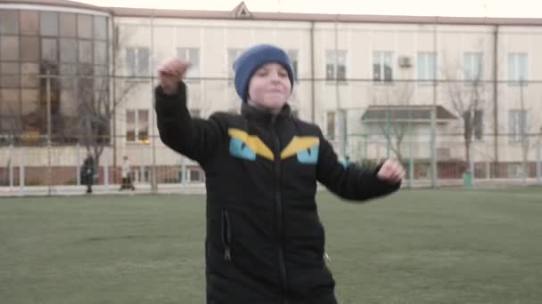 Niño alegre salta en el campo de fútbol verde contra la escuela Imágenes de stock libres de derechos