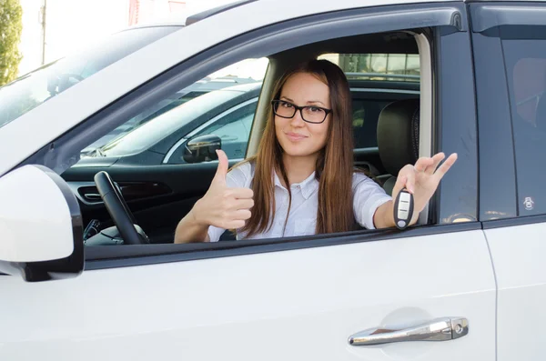 Mujer joven sentada en un coche nuevo y muestra las llaves de él — Foto de Stock