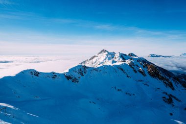 Soçi 'de bir dağın tepesinde, bulutların üstünde Rosa Tepesi. Karlı dağ sıraları ve güneşli mavi gökyüzü.