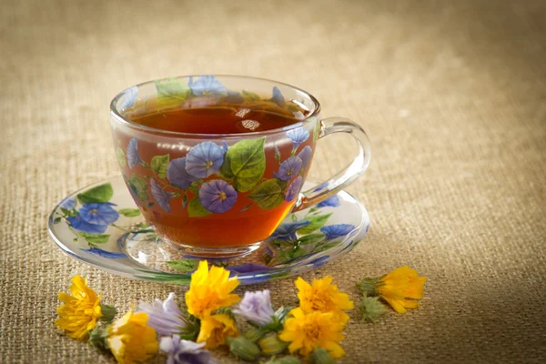 Glas Tee mit gelben und blauen Blüten — Stockfoto
