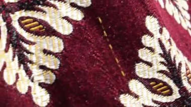 Süslü, bordo renkli kumaşın rüzgarda usulca hareket eden yakın plan görüntüsü beyaz ve sarı işlemeli tasarımları ortaya çıkarıyor. Yumuşak hareket güzel melodileri ortaya çıkarır..