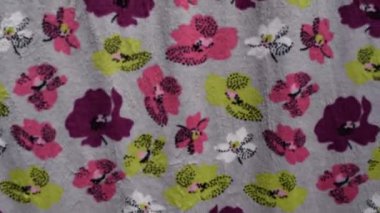  Yüksek çözünürlüklü video, rüzgarda hafifçe dalgalanan pembe, mor, beyaz ve limon yeşili çiçeklerin rüzgarla düzgün hareket ettiği renkli çiçek desenli yumuşak gri bir kumaşı gösteriyor. Geçmişler için kullanışlı