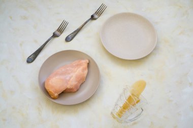 Masaya şeffaf bir bardaktan dökülen çatallar ve iki tabak çiğ tavuk filetosu kahvaltı ya da öğle yemeği için hazırlanır.